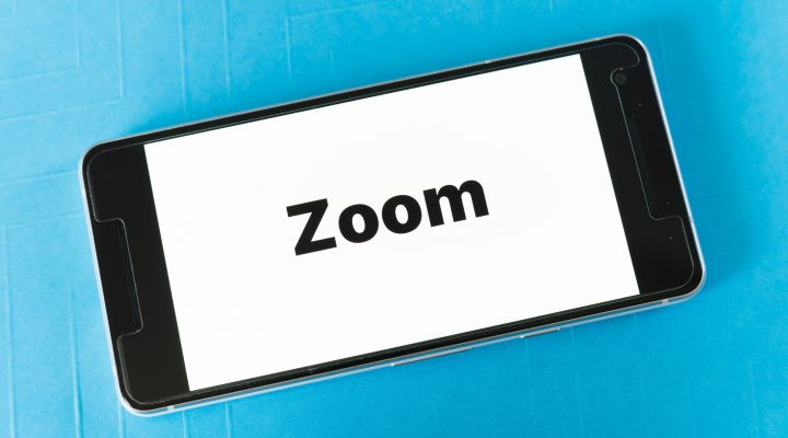 a cell phone with the word Zoom in bold on it laying against a blue background